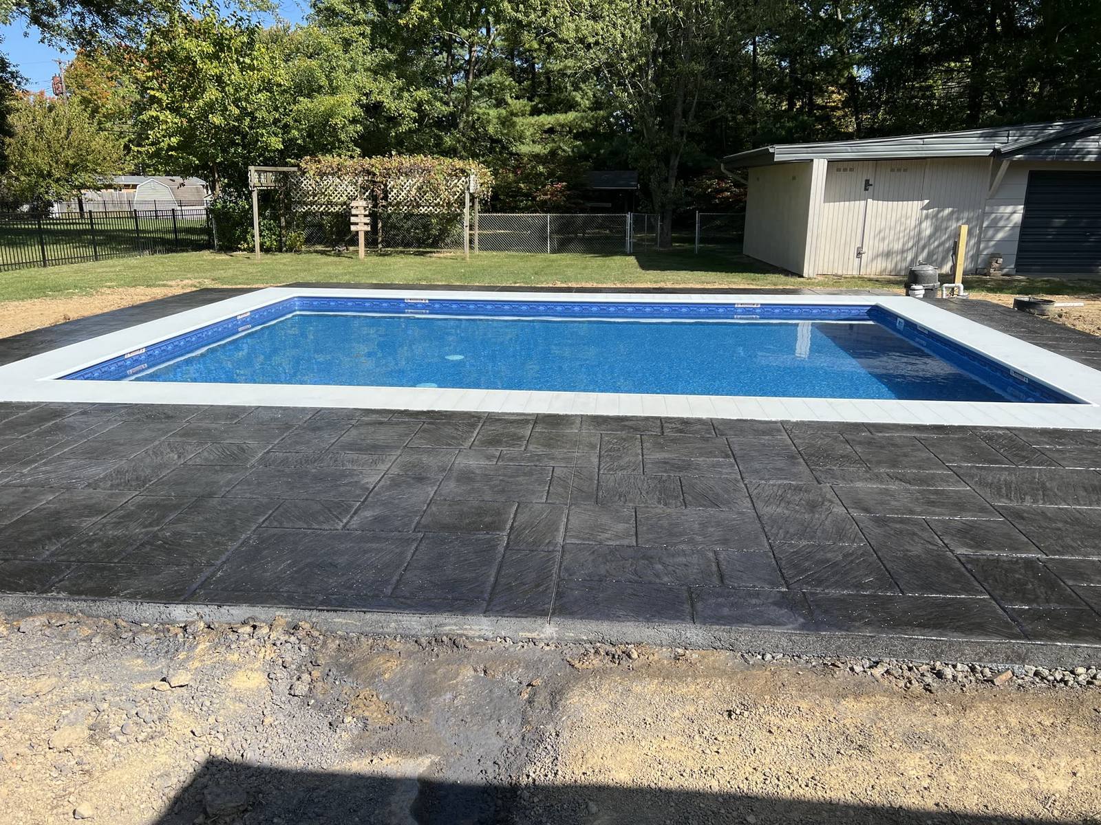 Dark stamped concrete pool patio with stone-pattern finish in bright daylight
