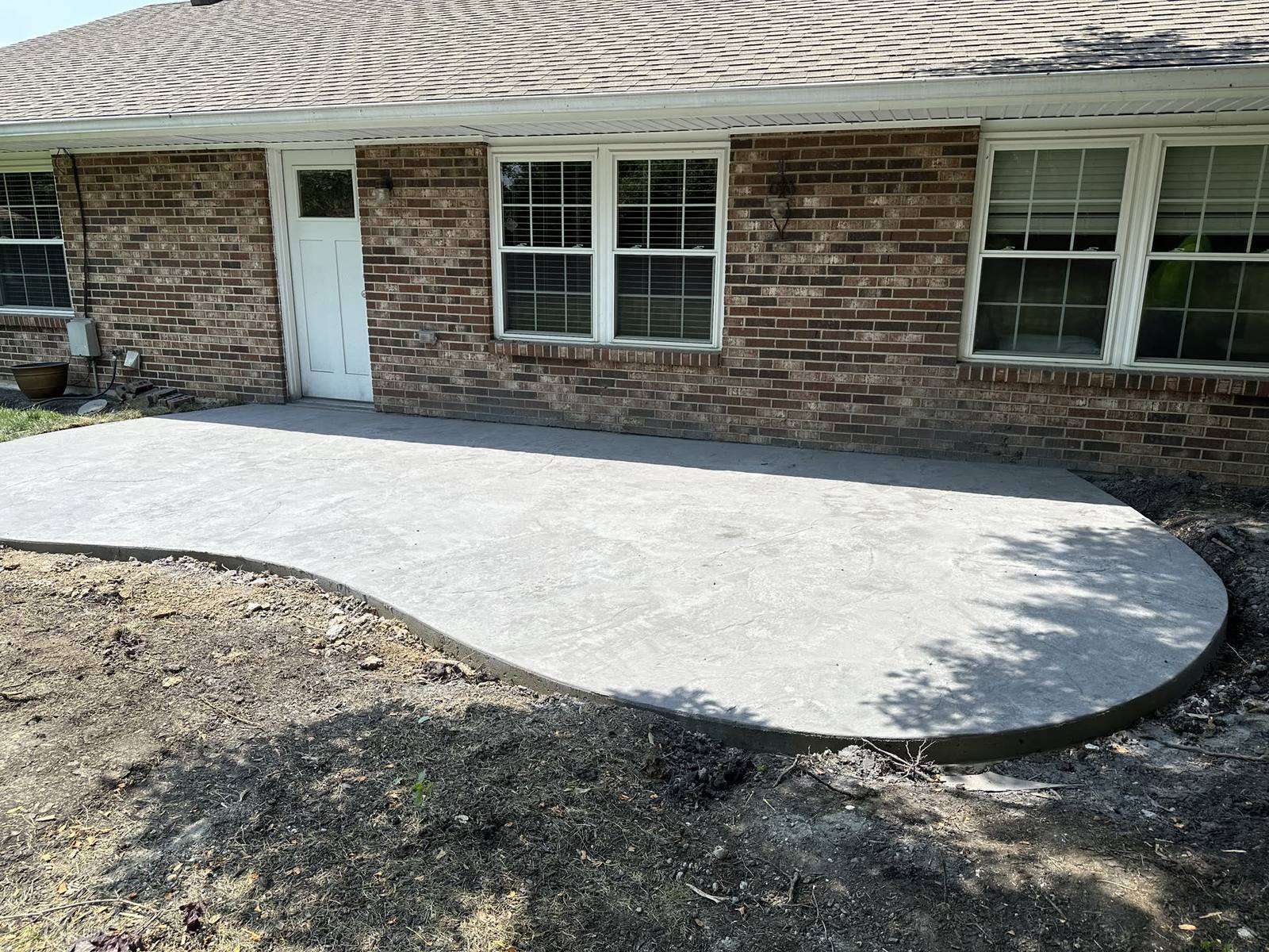 Curved light-gray concrete patio installation at a brick home in Southwest Ohio