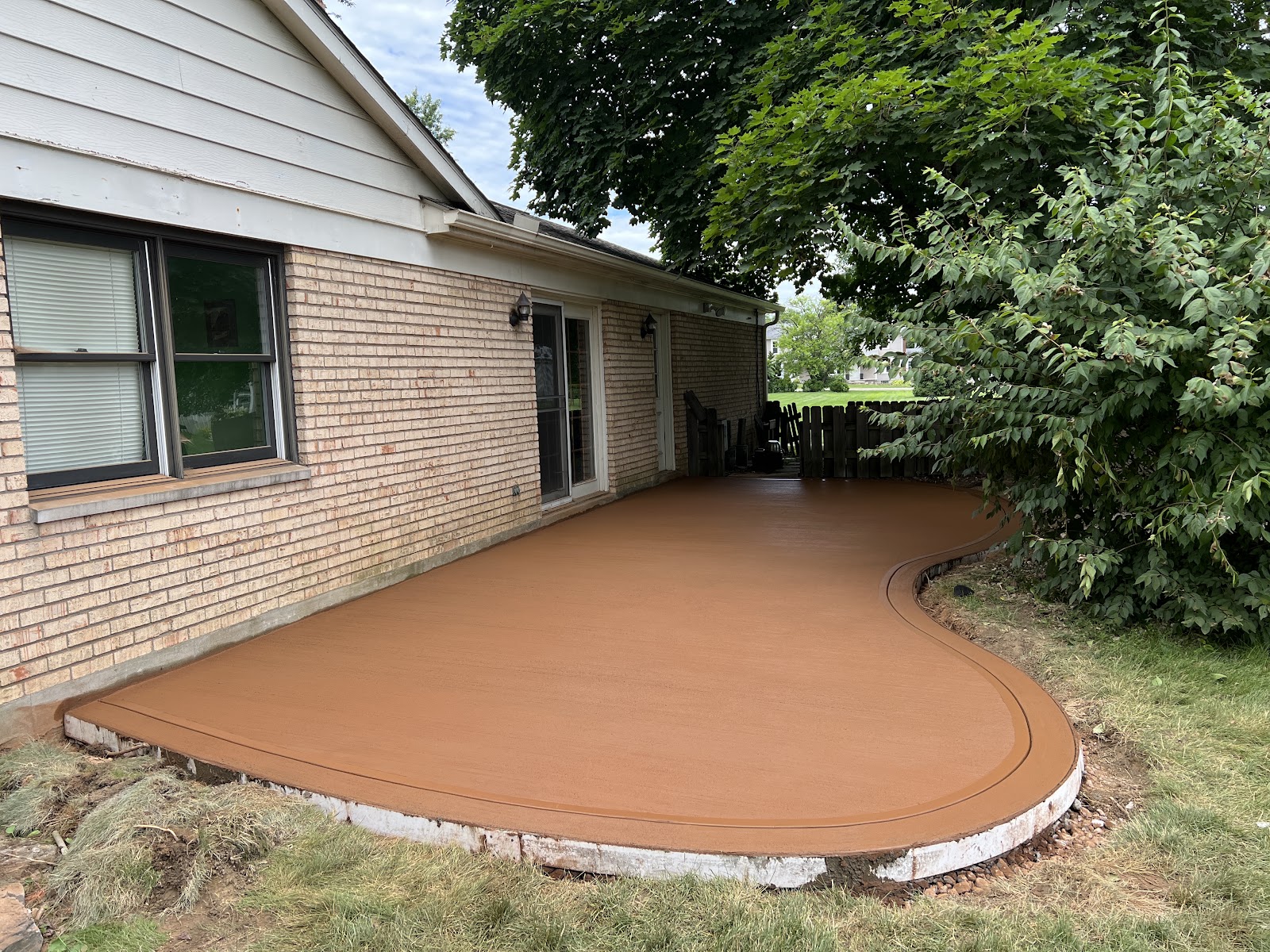 Curved amber-stained concrete patio with a dark accent border along a brick ranch home