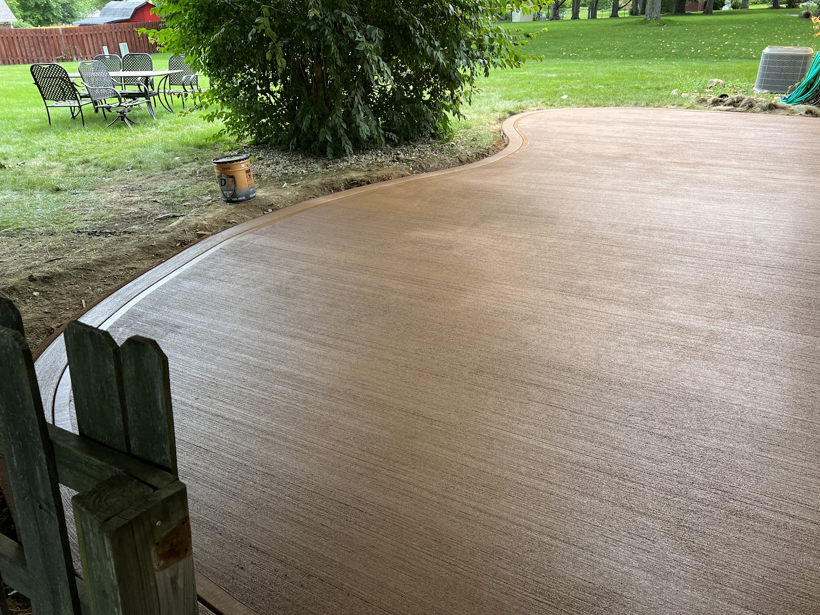 Curved tan concrete patio with a decorative border, freshly poured behind a home