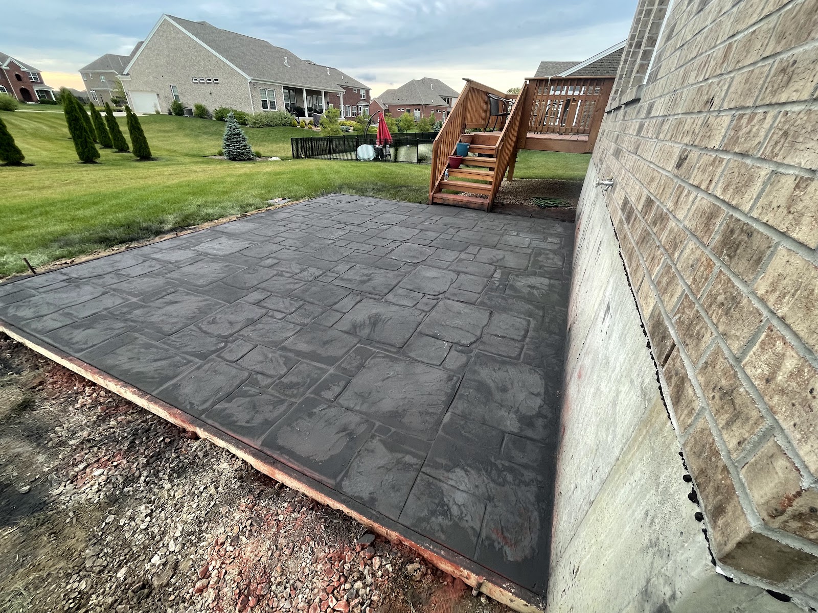 Charcoal stamped concrete patio with an ashlar pattern beside a deck staircase