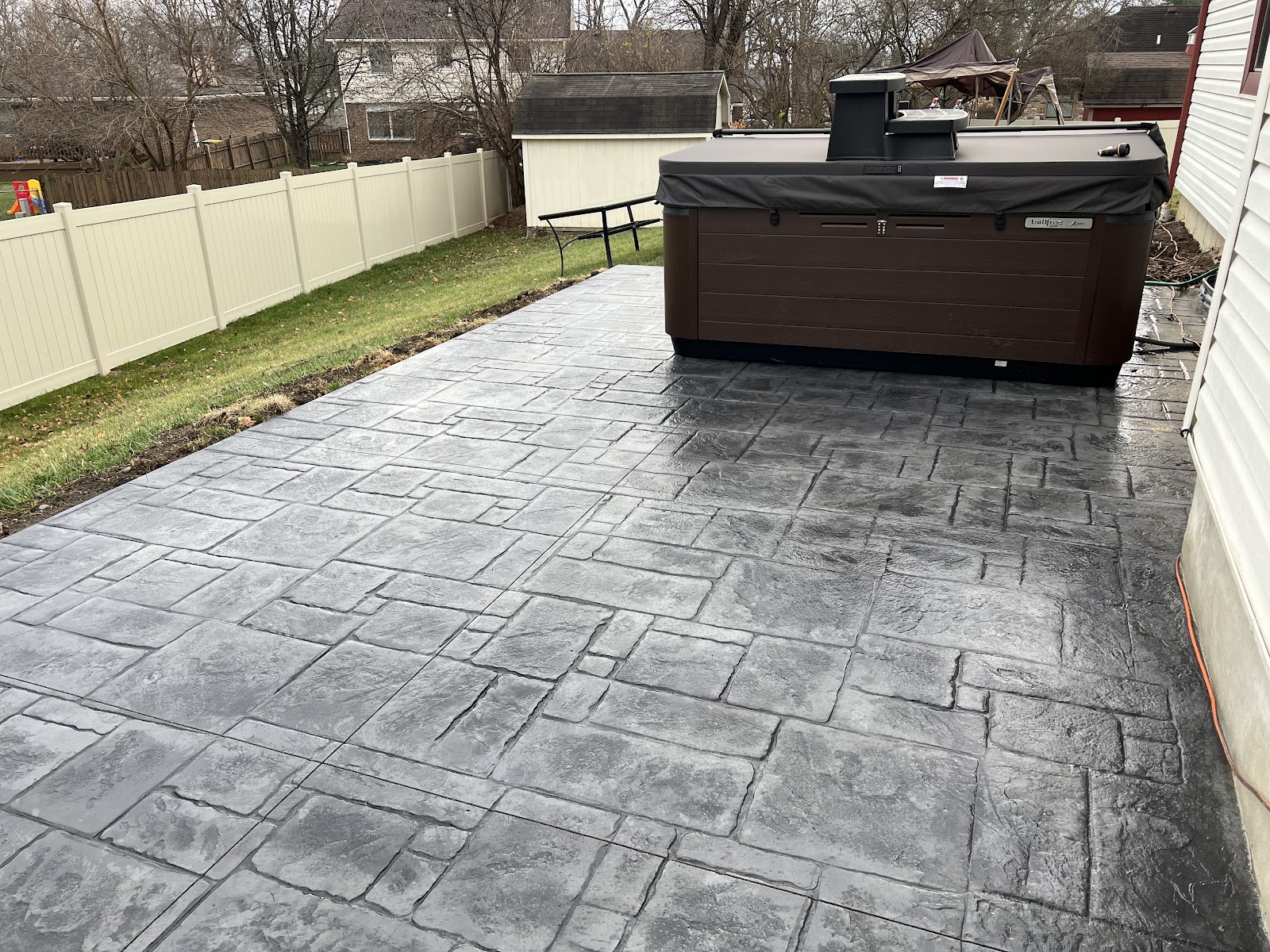 Charcoal stamped concrete patio built out for a hot tub pad in a fenced backyard